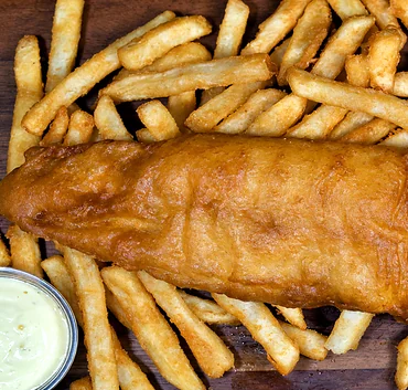 Battered halibut fillet on fries with a lemon wedge and tartar sauce