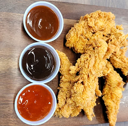 Chicken tenders on a wooden board with three dipping sauces