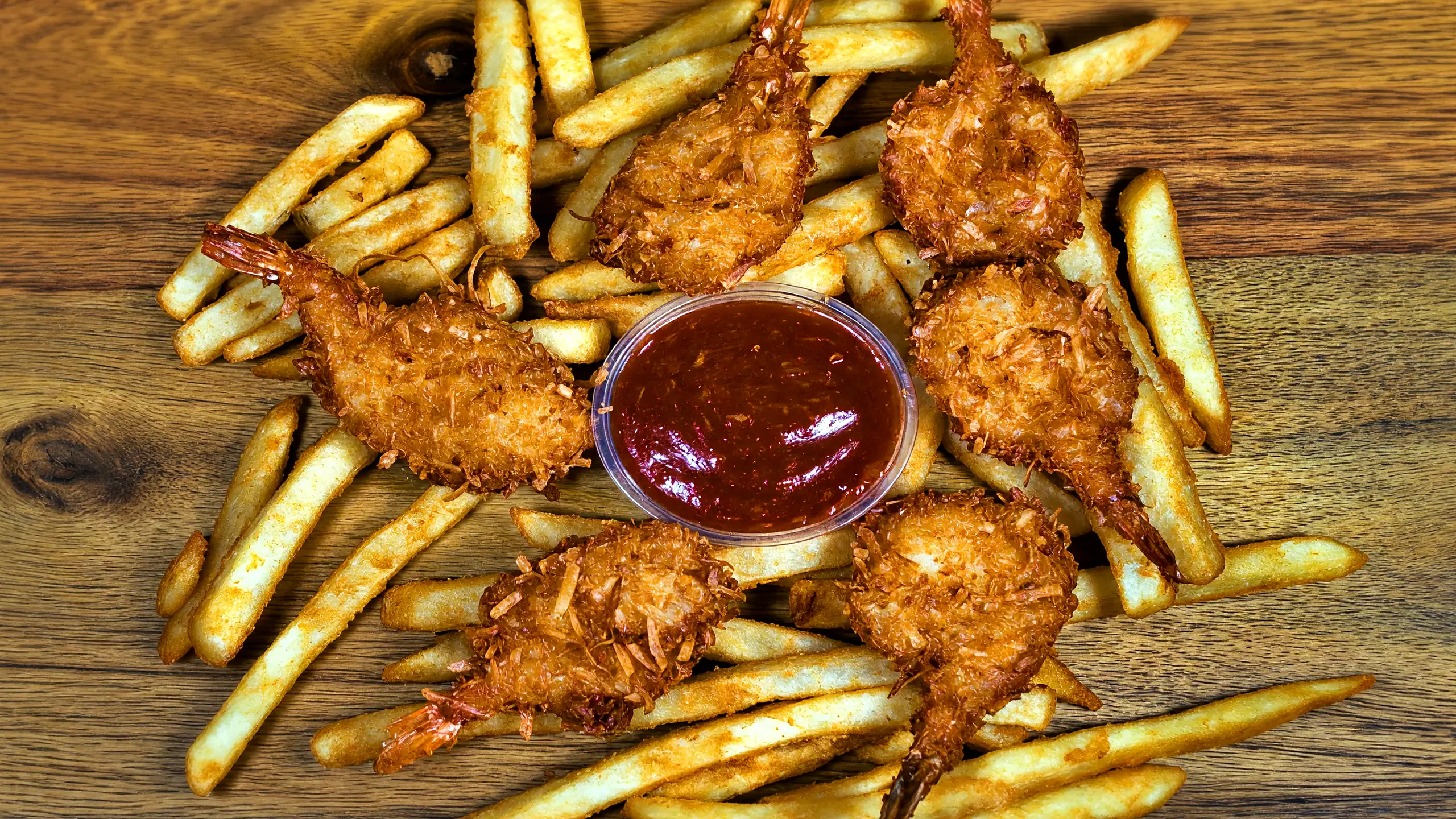 Breaded jumbo shrimp on fries around a cup of cocktail sauce