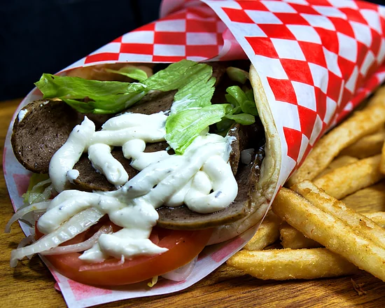 Gyro wrap with sliced meat, lettuce, tomato and garlic sauce, beside fries